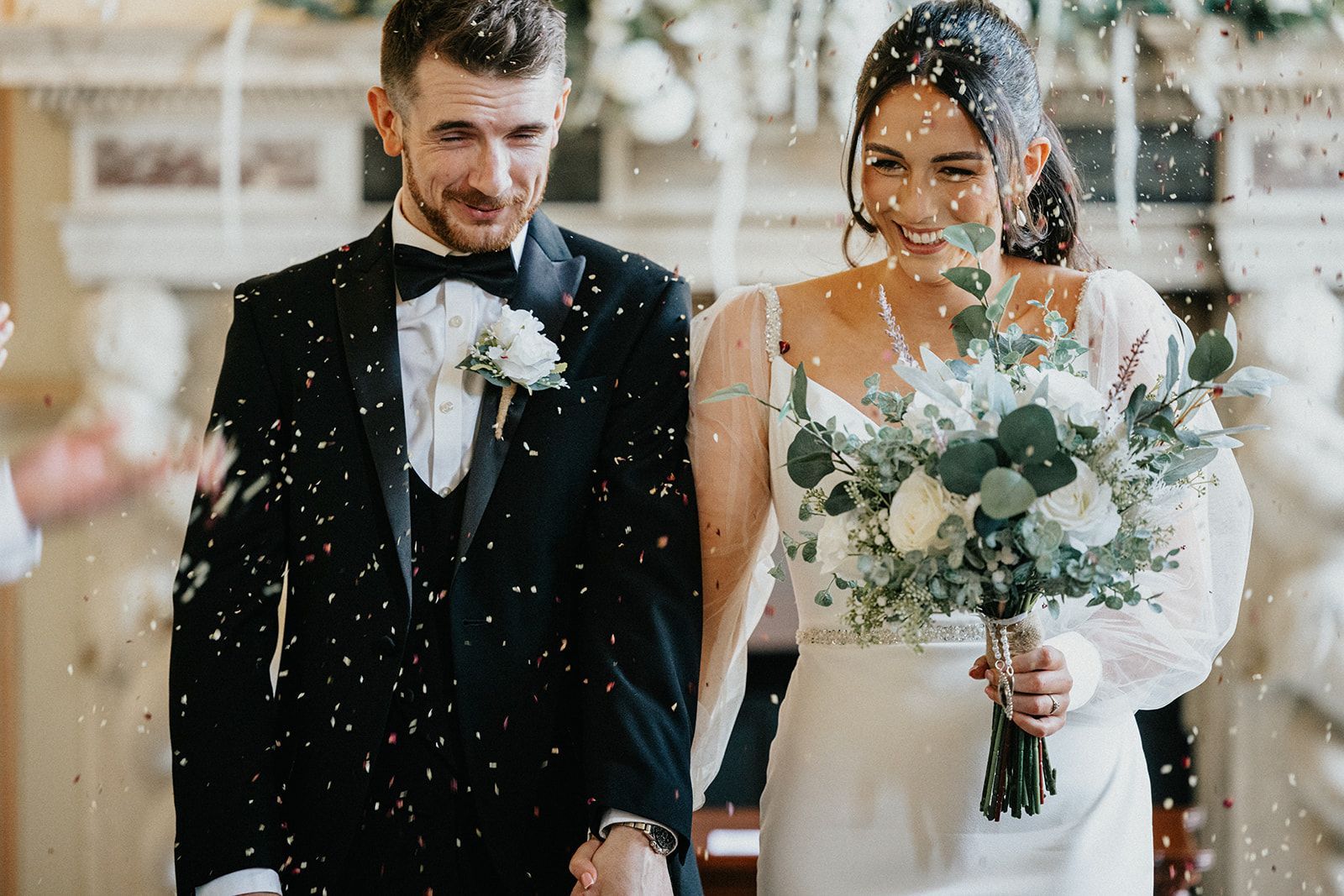 A bride and groom are walking down the aisle with confetti being thrown at them.