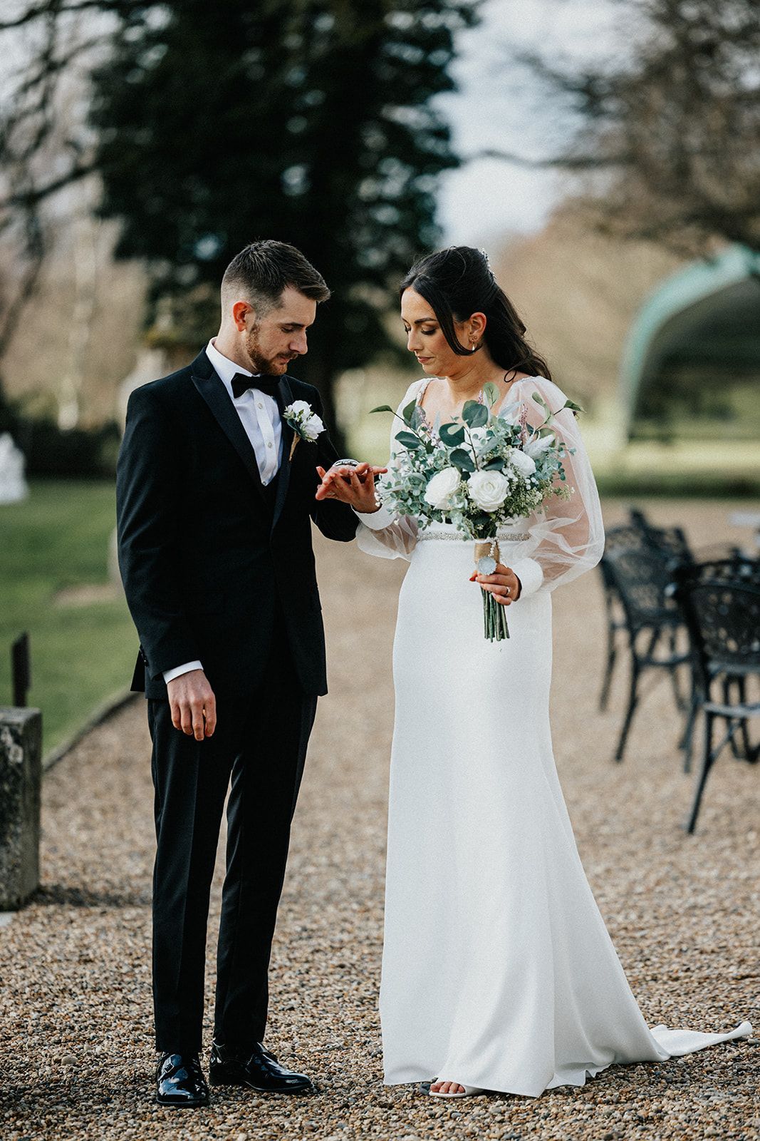 A bride and groom are standing next to each other on a gravel road.