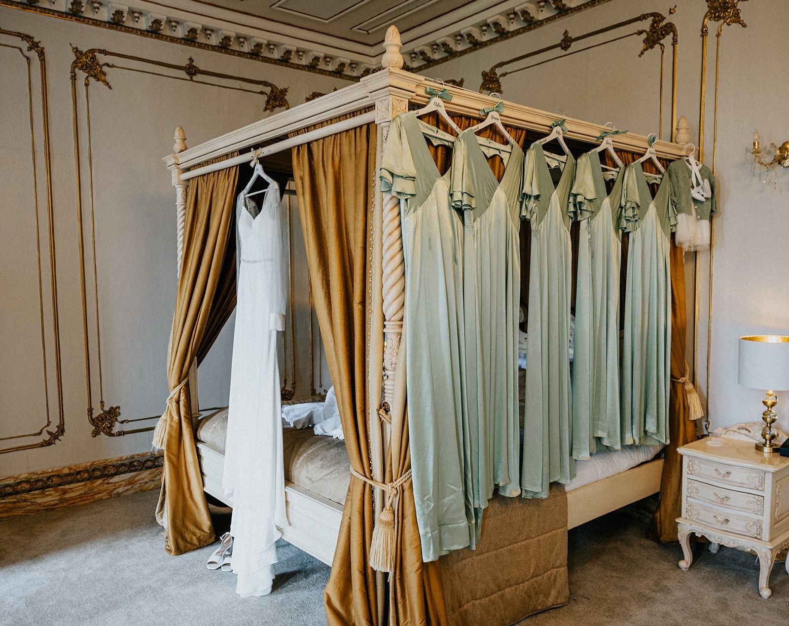 A four poster bed with dresses hanging on it in a bedroom.