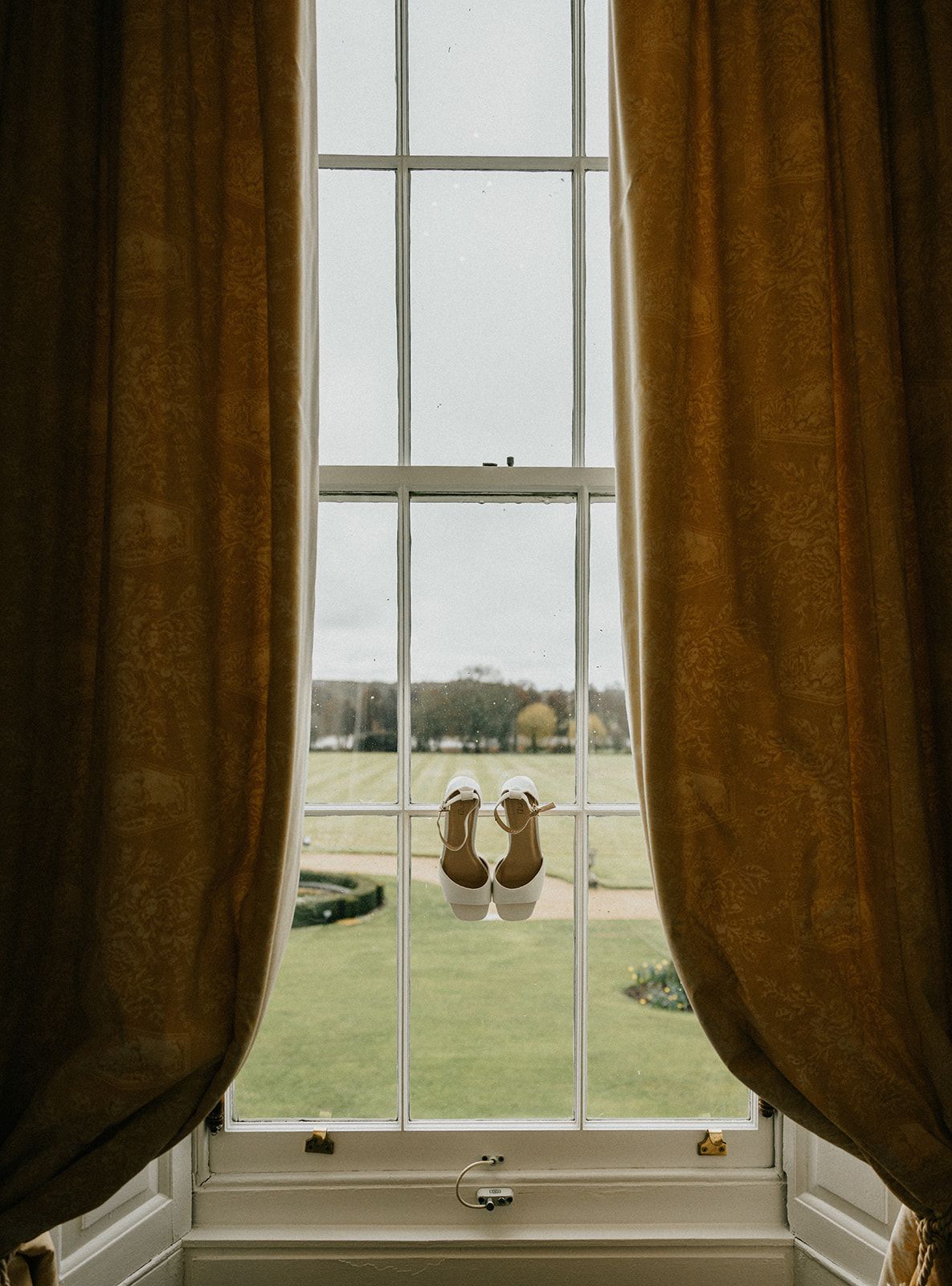 A pair of wedding shoes are hanging out of a window.
