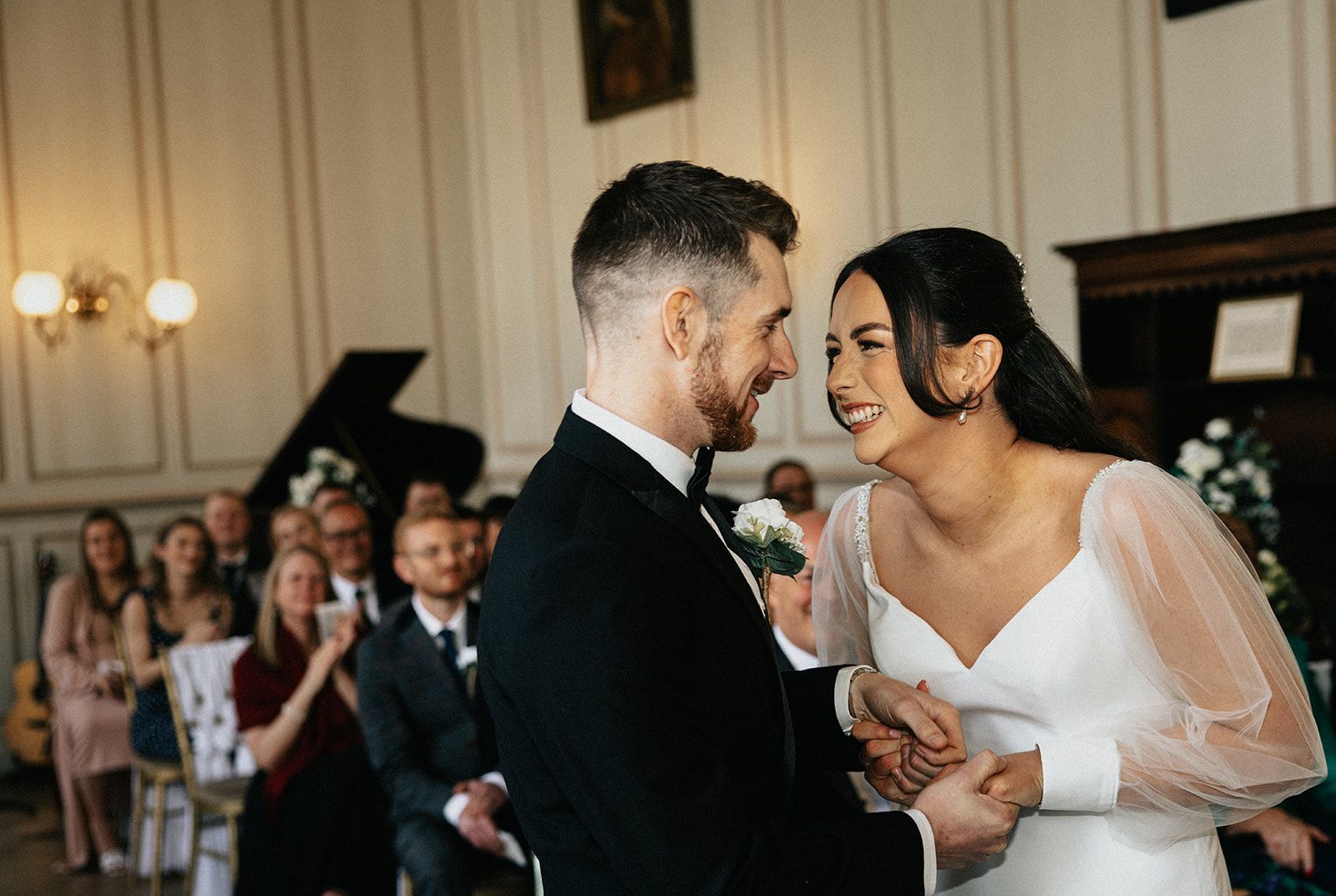 A bride and groom are smiling at each other during their wedding ceremony.