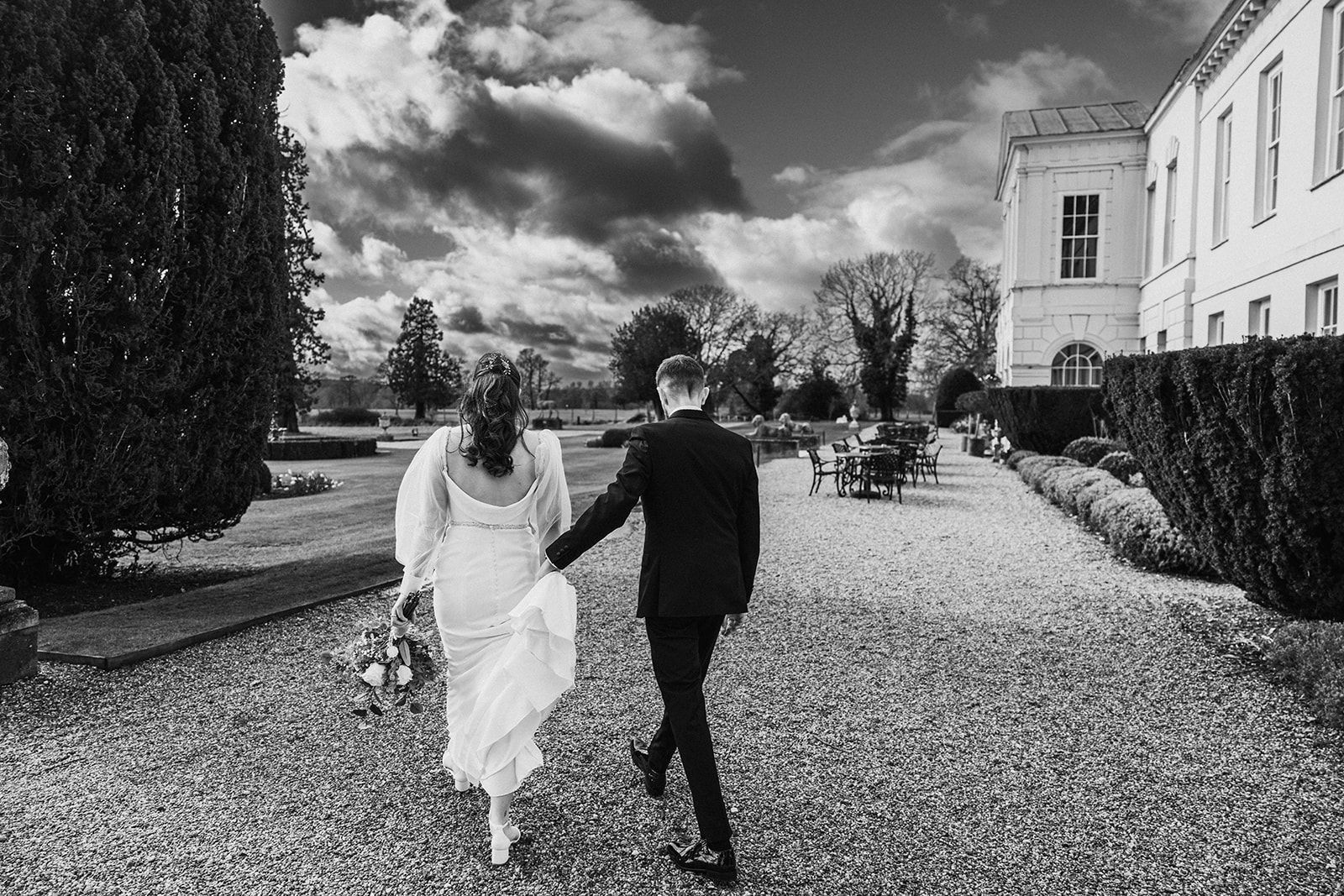 A bride and groom are walking down a gravel path in front of a large building.