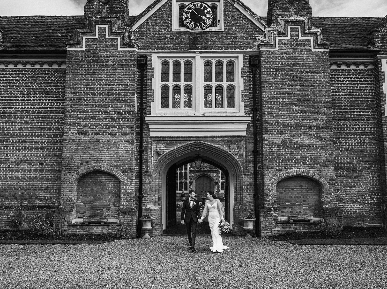 A black and white photo of a bride and groom standing in front of a brick building.