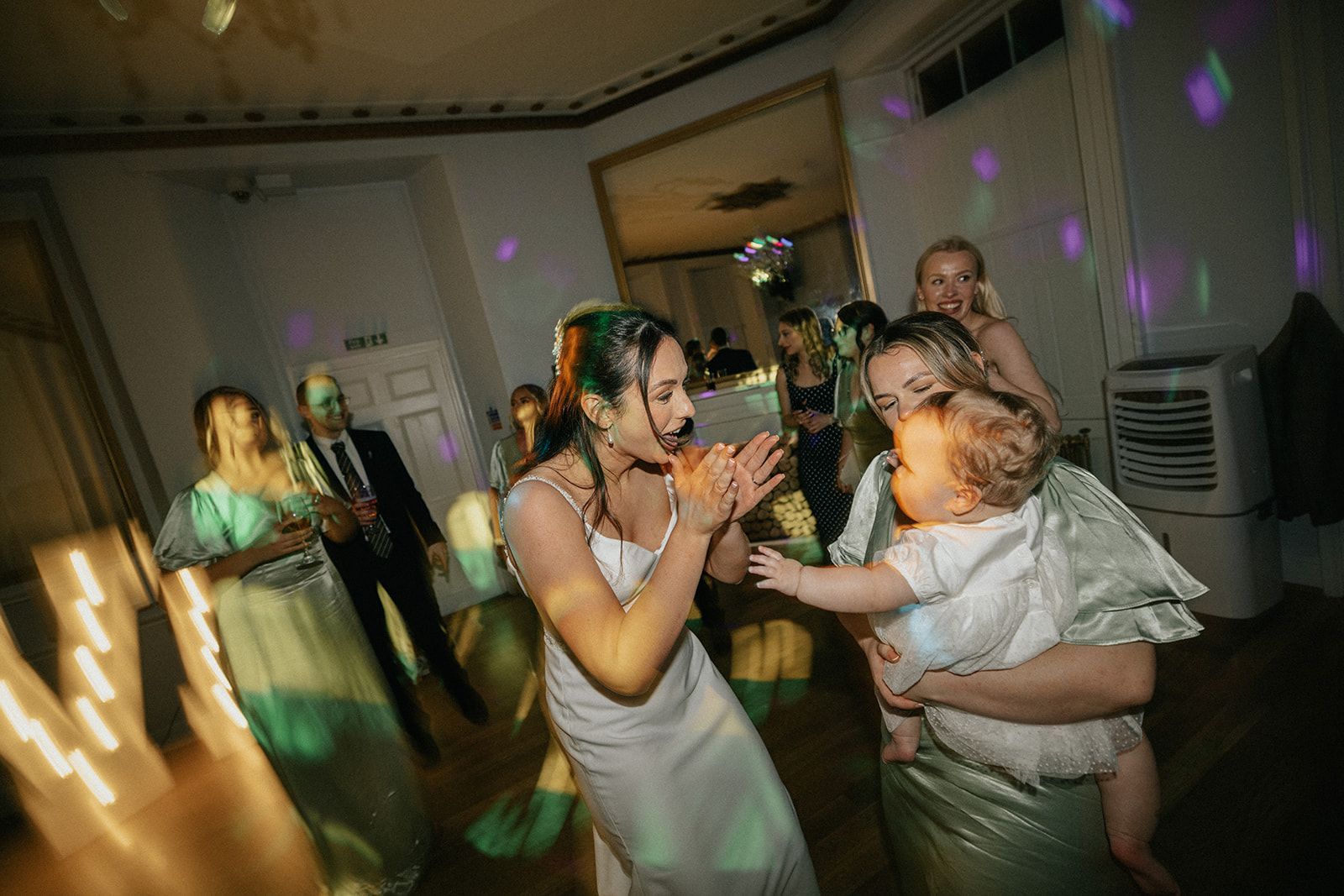 A woman is holding a baby while dancing at a wedding reception.