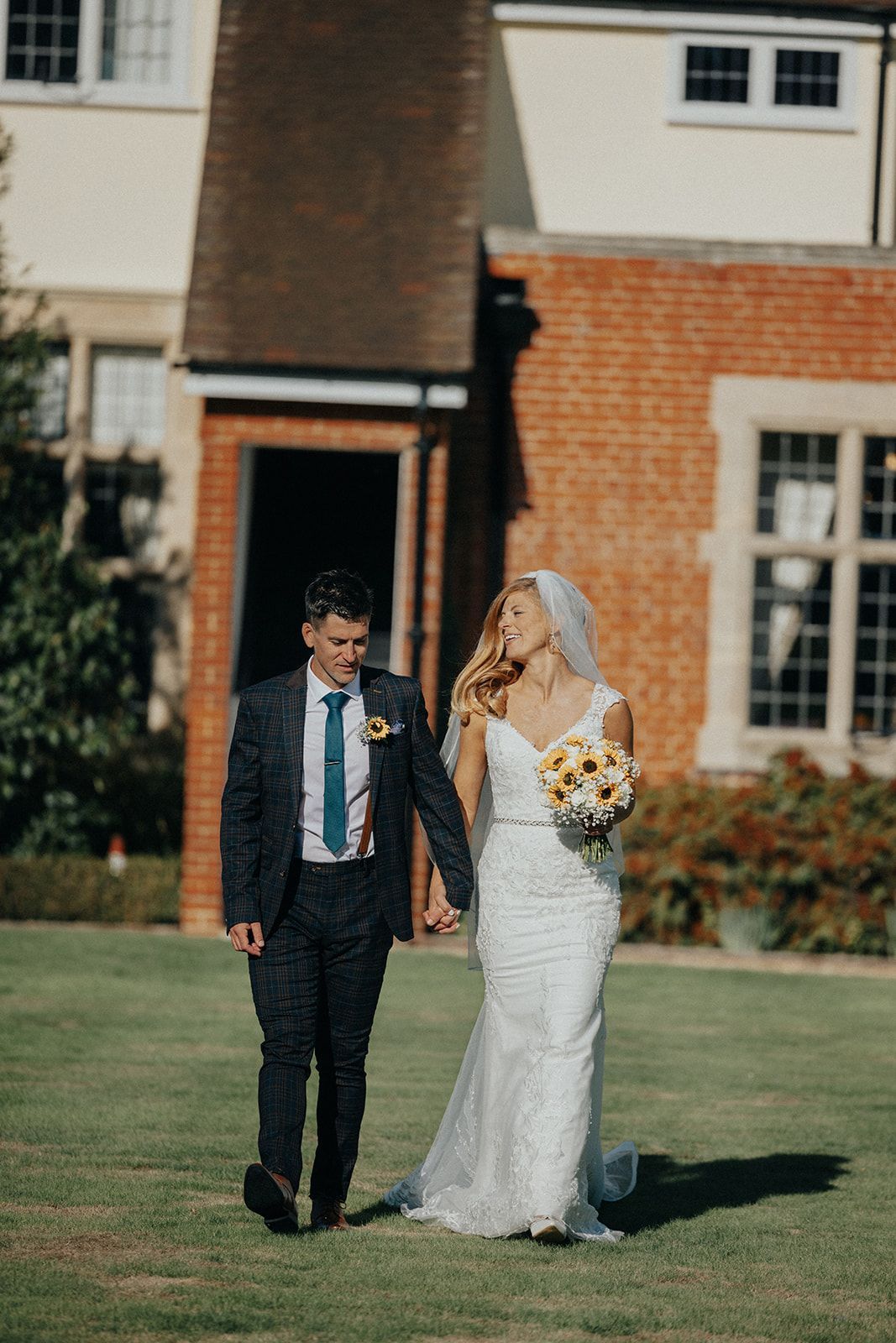 A bride and groom are walking in front of a brick building holding hands.