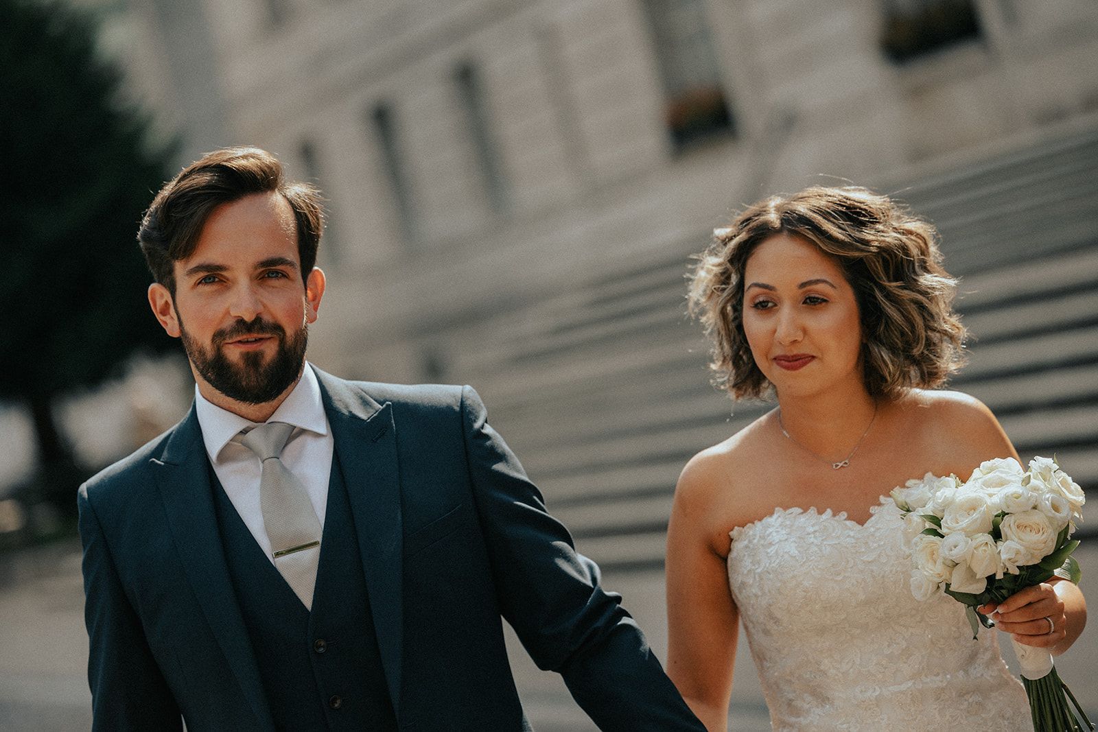 A bride and groom are walking down a set of stairs holding hands.