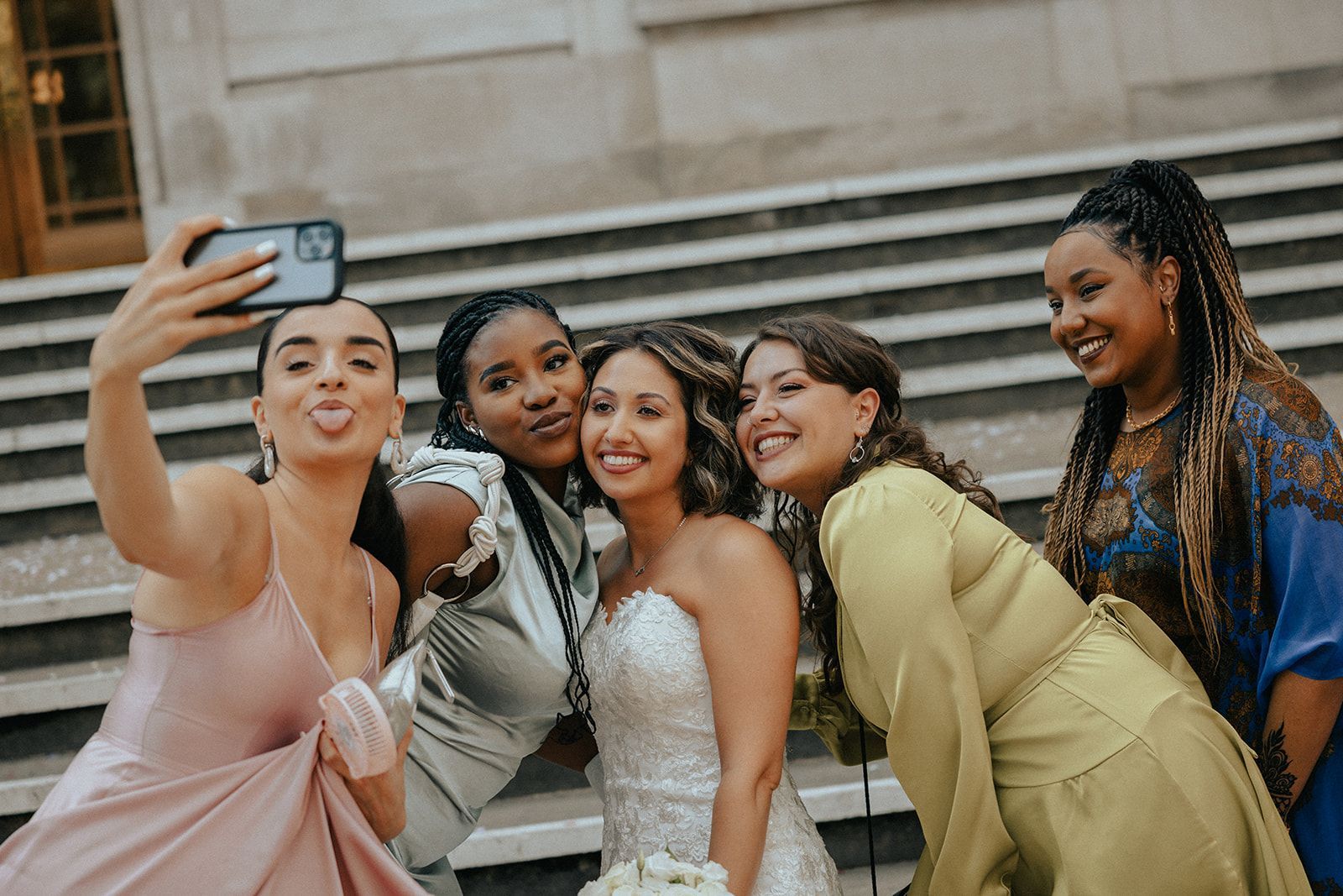 A bride and her bridesmaids are taking a selfie together.