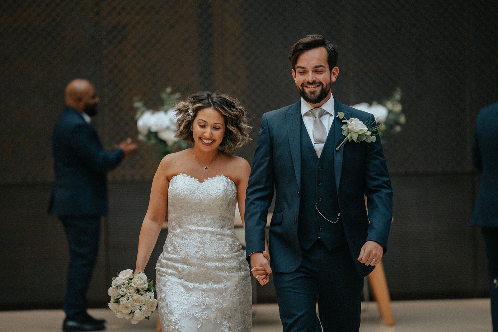 A bride and groom are walking down the aisle holding hands.