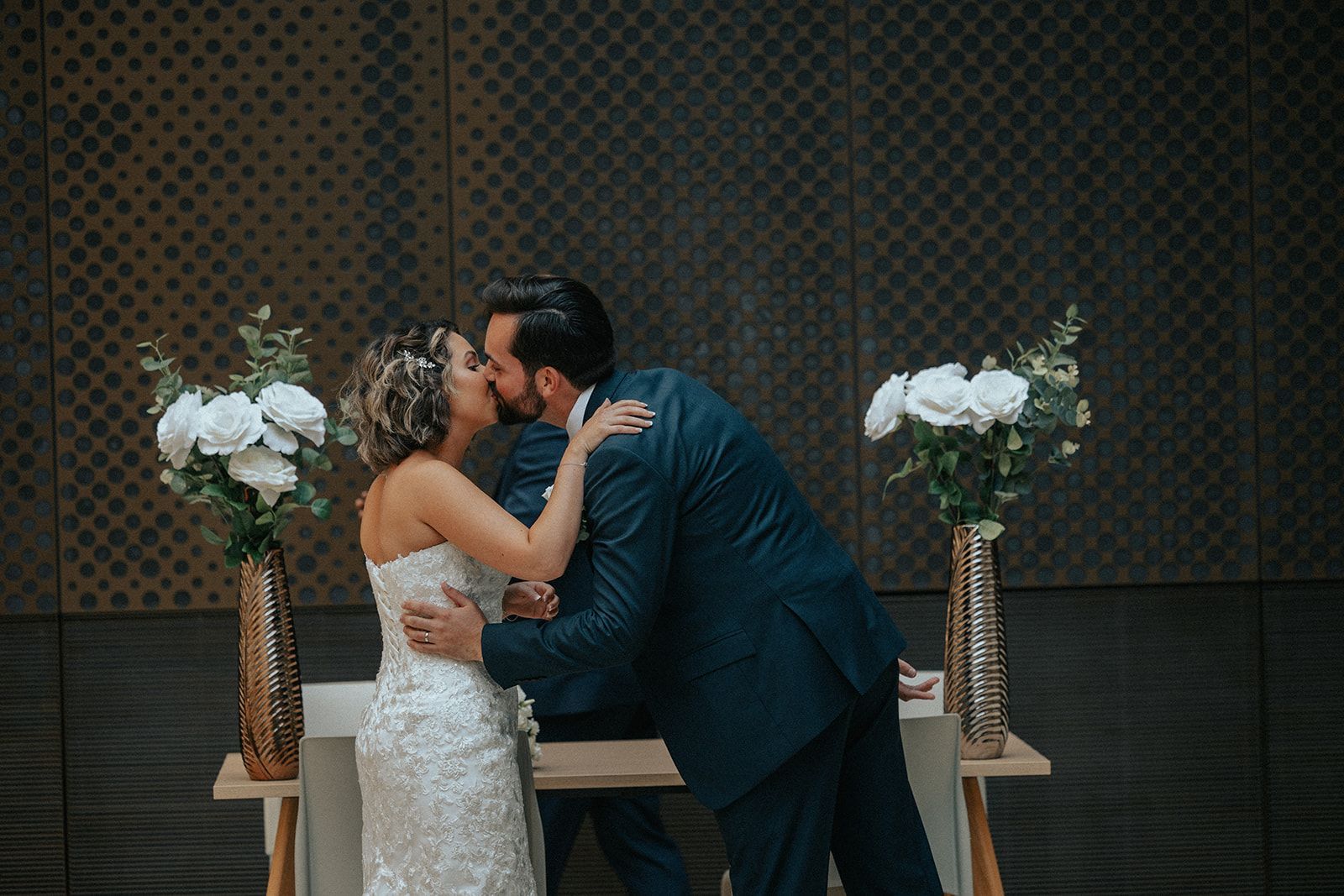 A bride and groom are kissing during their wedding ceremony.