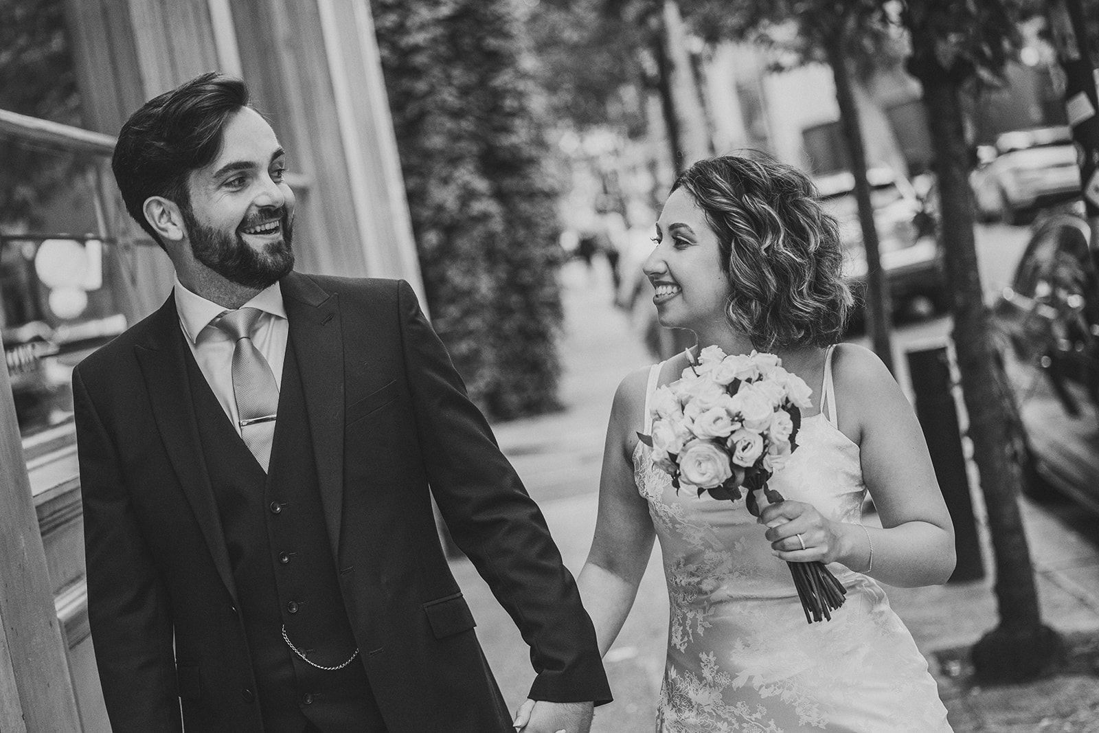 A bride and groom are walking down the street holding hands.