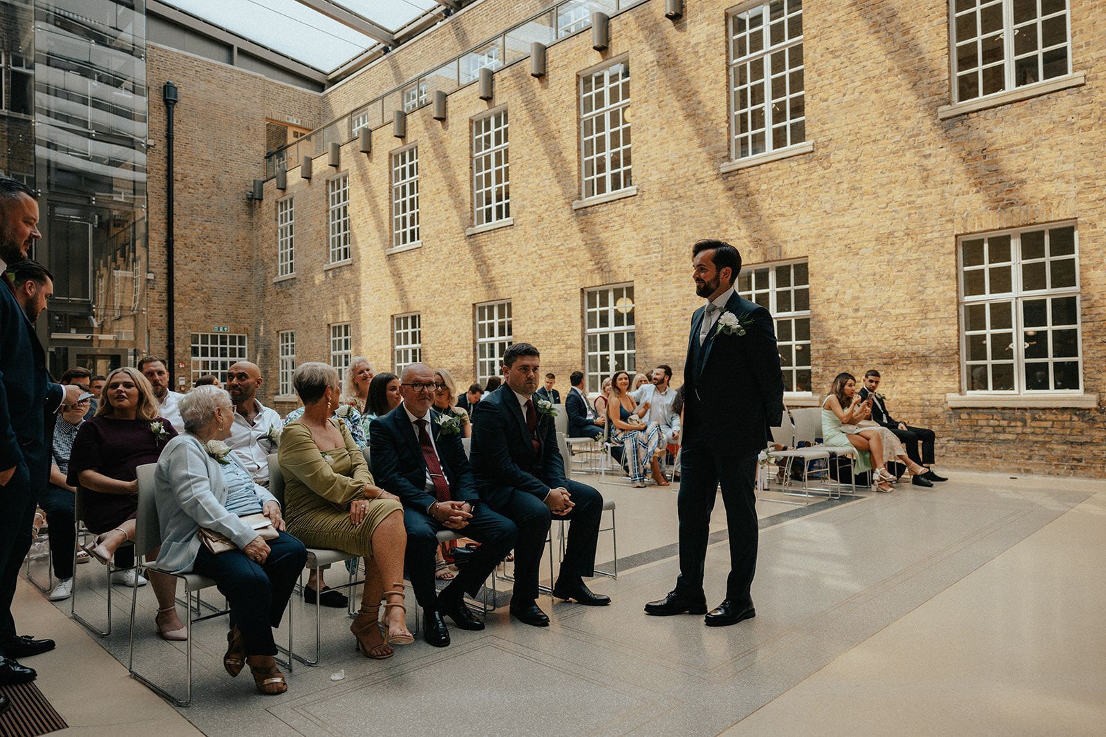 A man in a suit is standing in front of a crowd of people at a wedding ceremony.