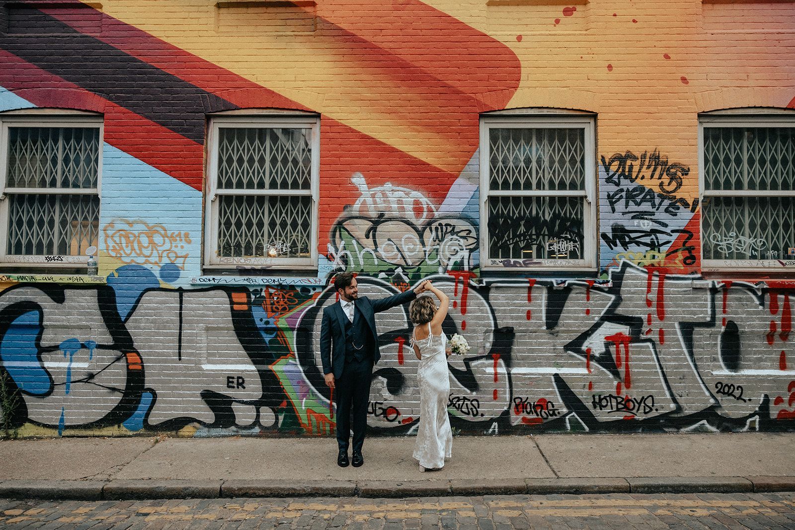 A bride and groom are standing in front of a graffiti covered wall.