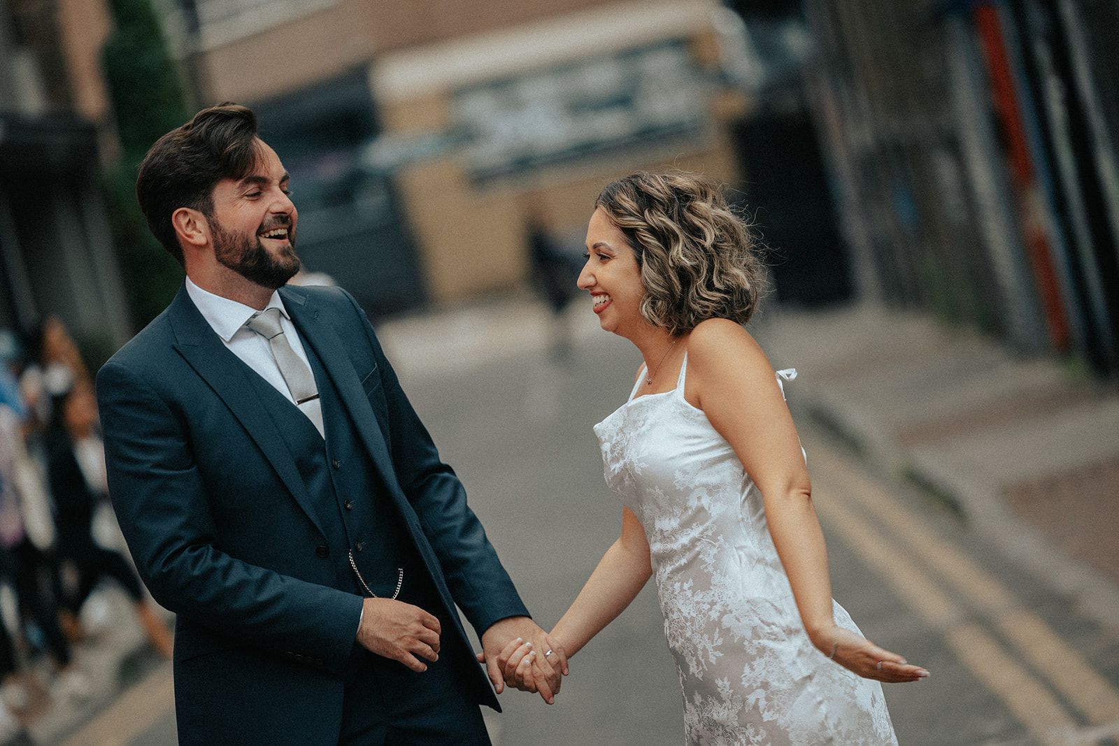 A bride and groom are holding hands on a city street.