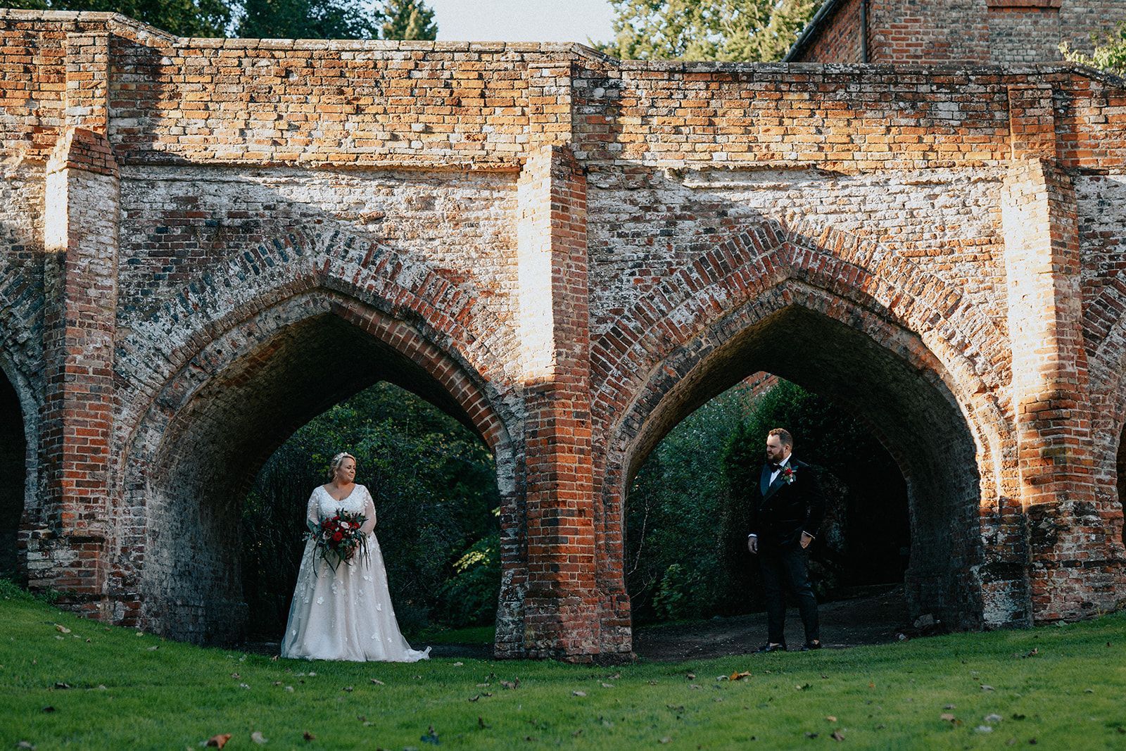 A bride and groom are standing under a brick archway.