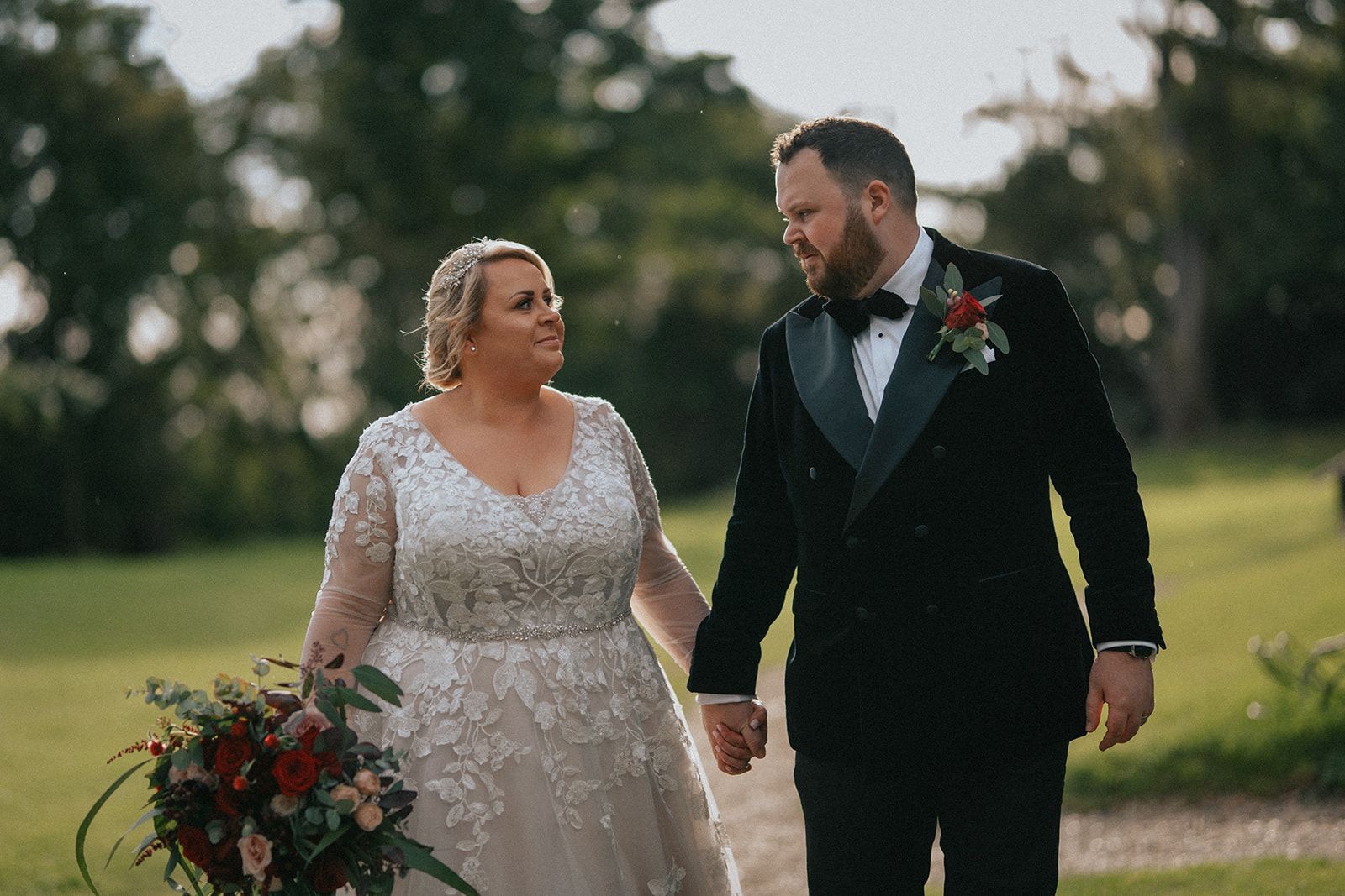A bride and groom are walking down a path holding hands.