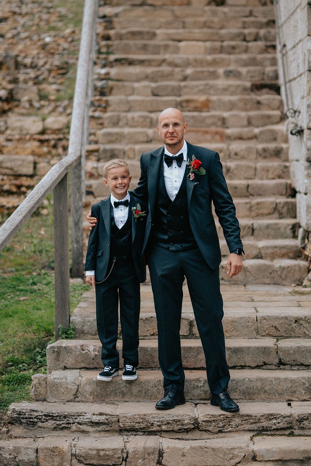 A man and a boy in tuxedos are standing on a set of stairs.