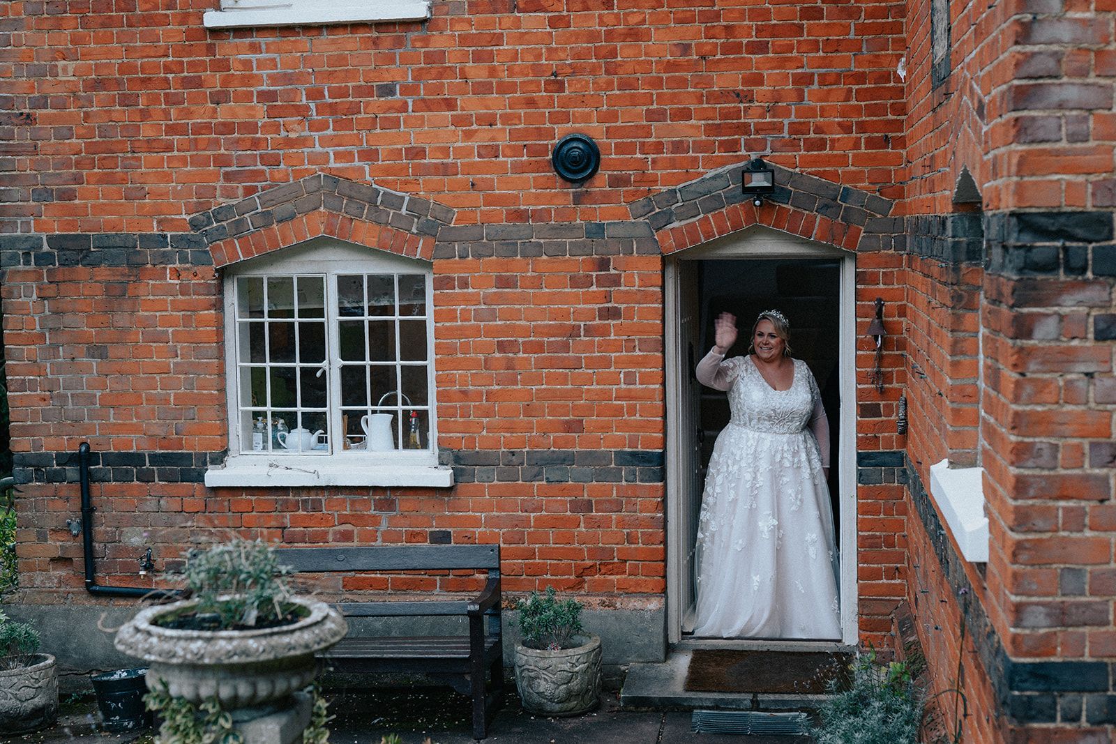 A bride in a wedding dress is standing in the doorway of a brick building.