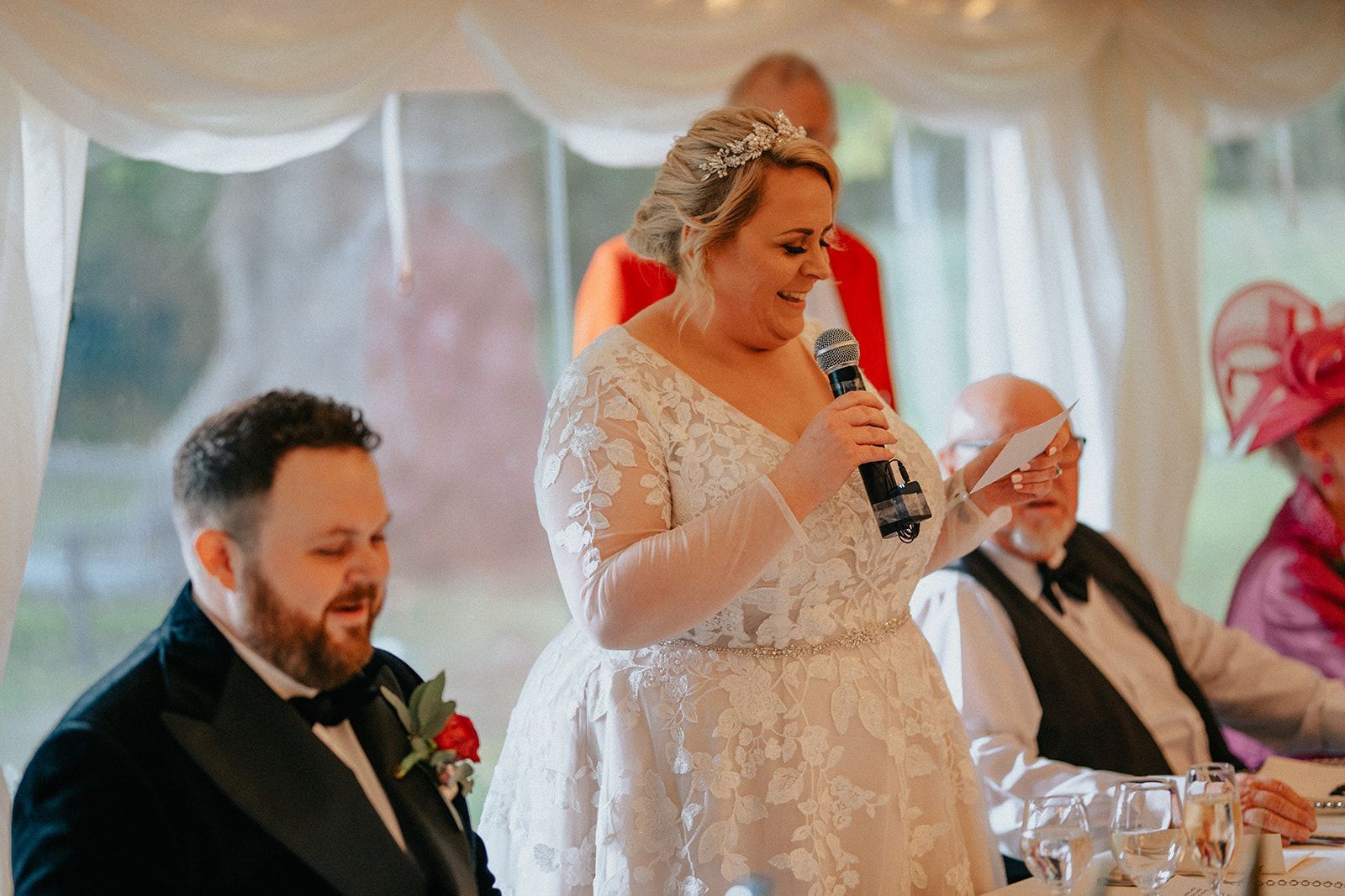A bride and groom are sitting at a table while the bride is holding a microphone.