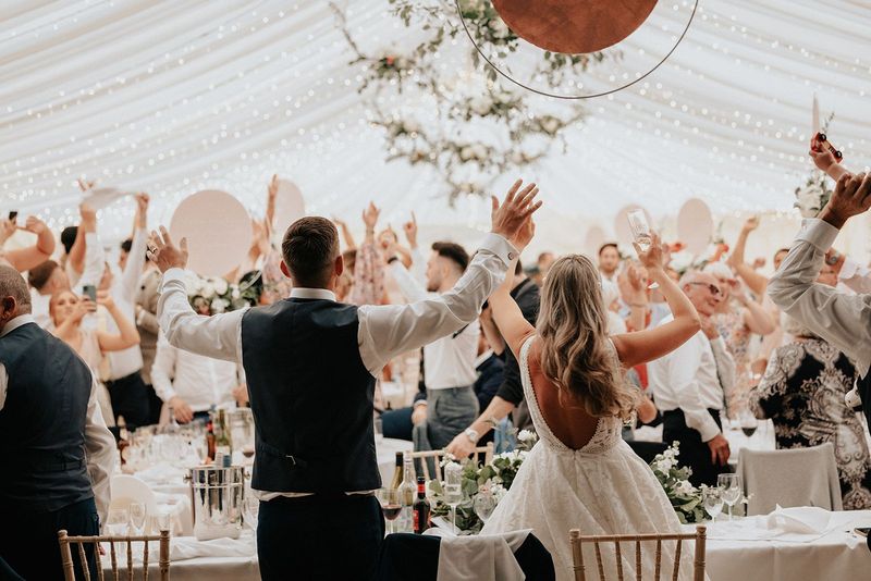 a bride and groom are dancing at their wedding reception with their hands in the air .