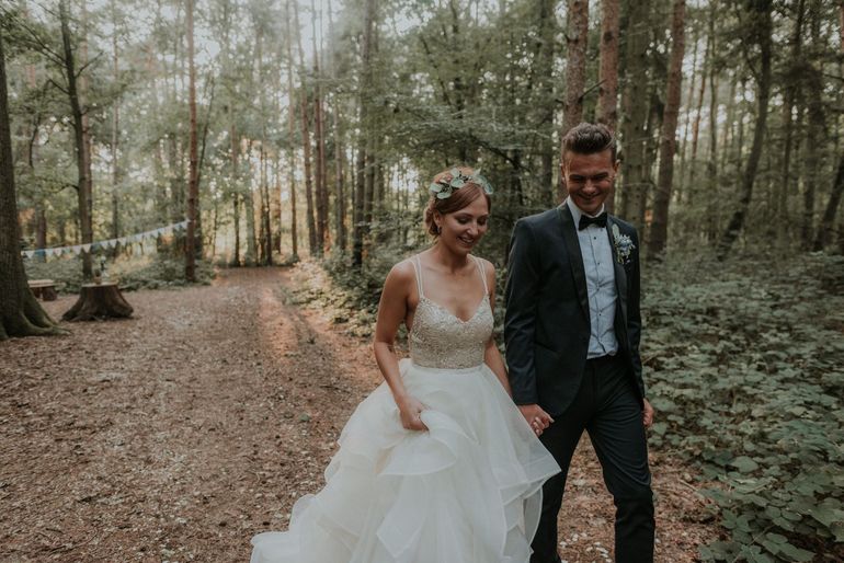 a bride and groom are walking through the woods holding hands .