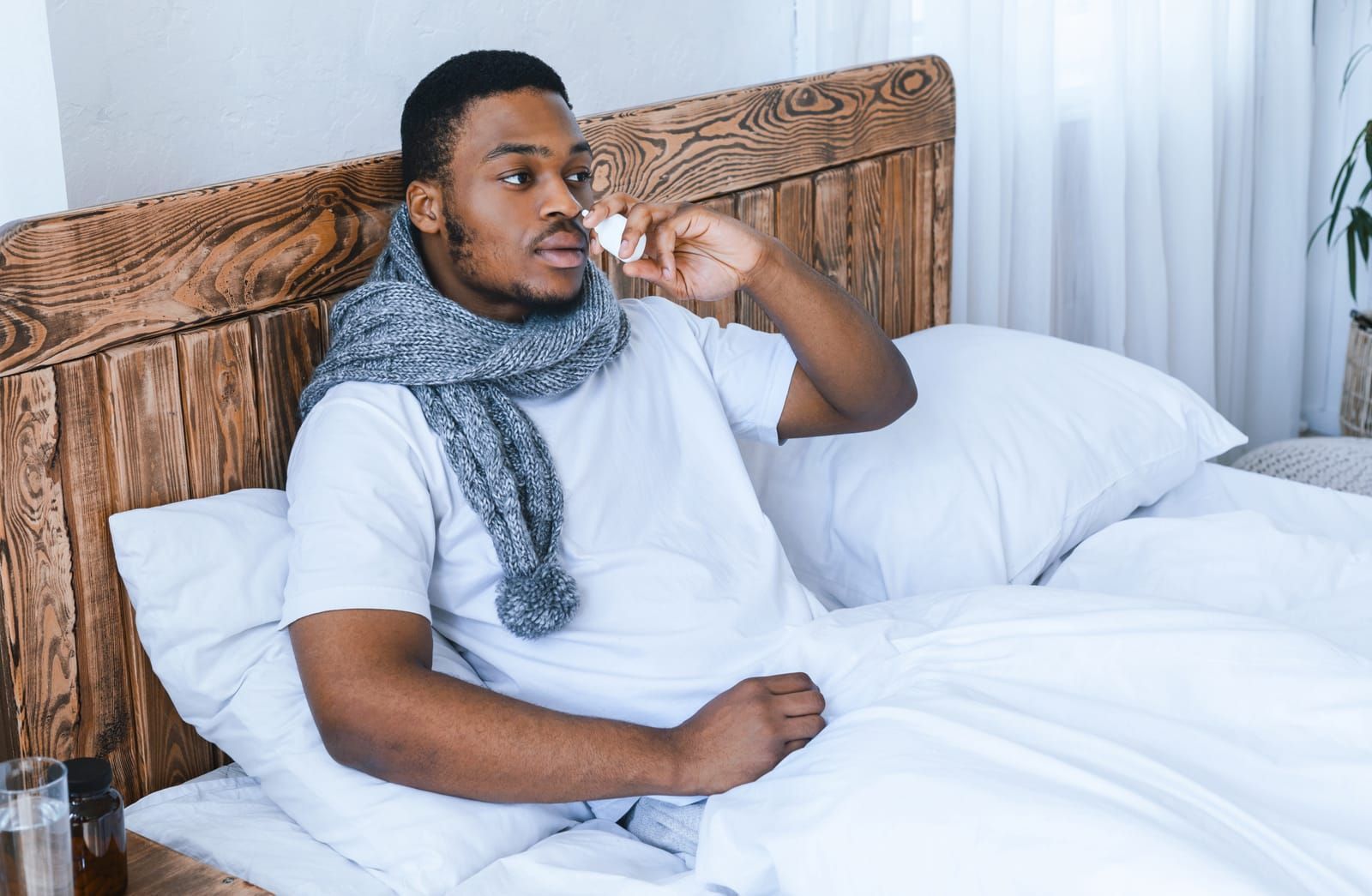 man-suffering-from-dry-nose-using-nasal-spray-sitting-in-bed