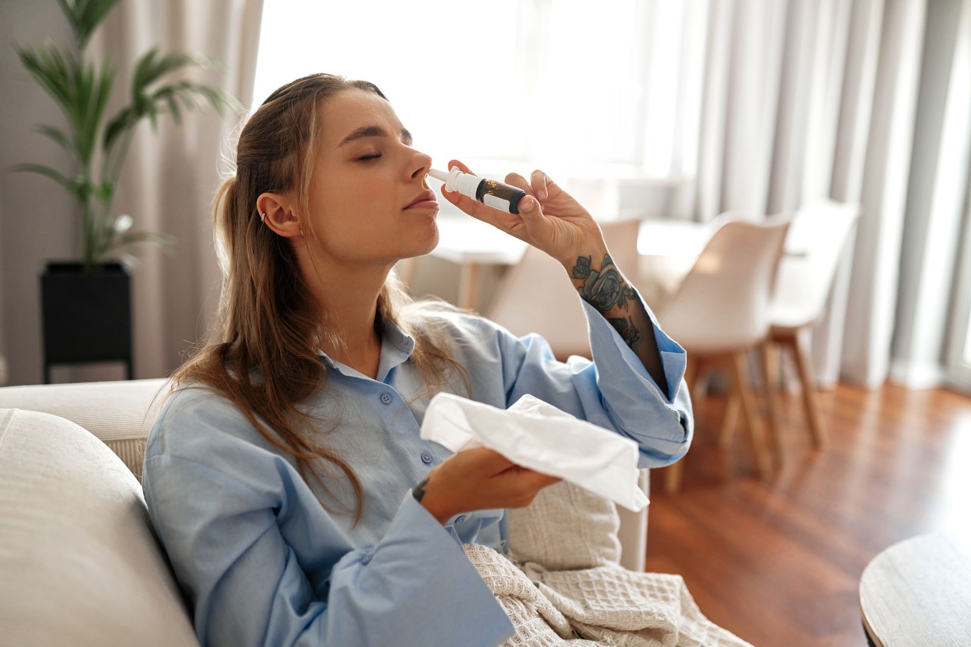 A woman is sitting on a couch using a nasal spray.