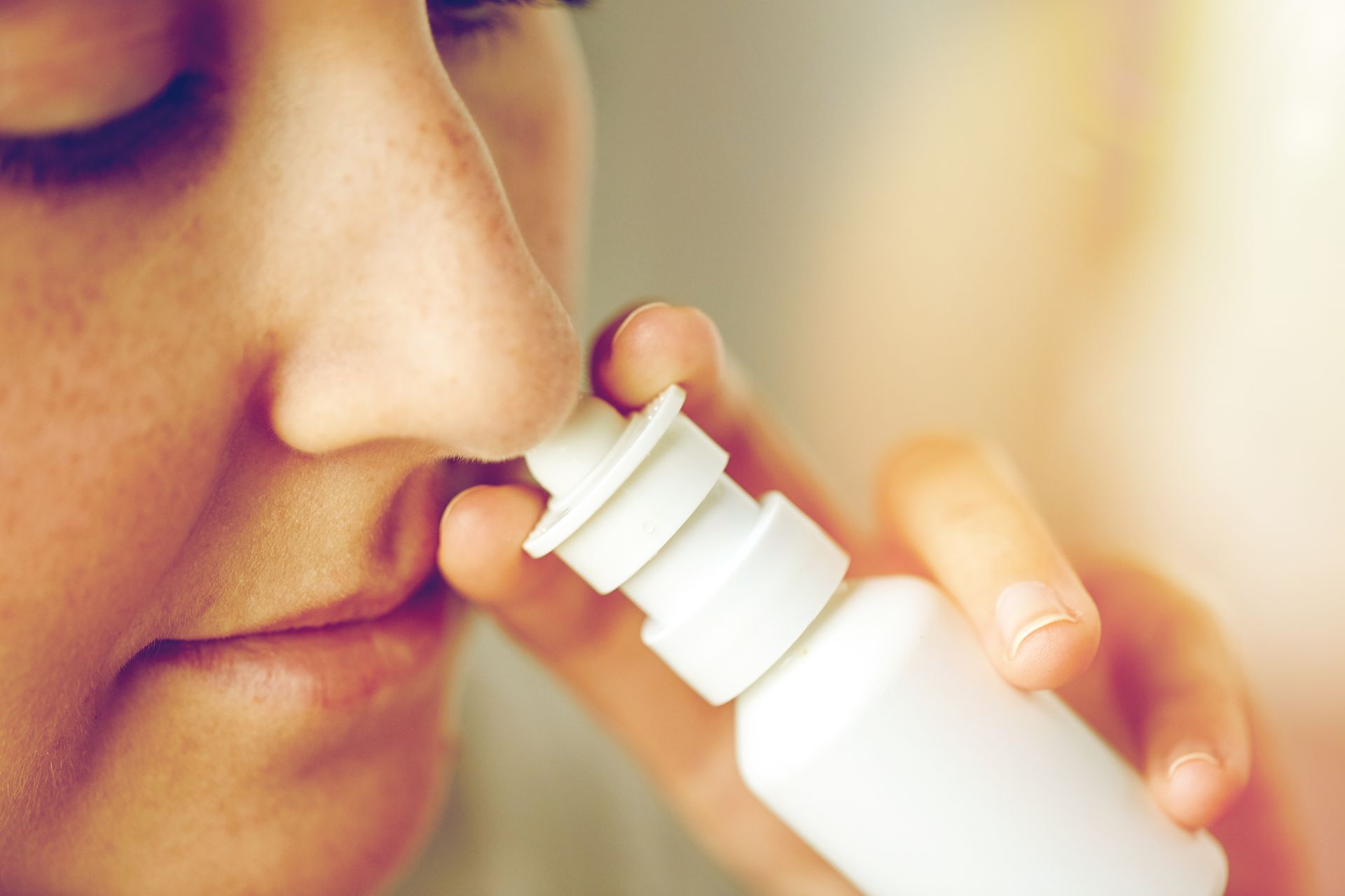 A woman is using a nasal spray in her nose.