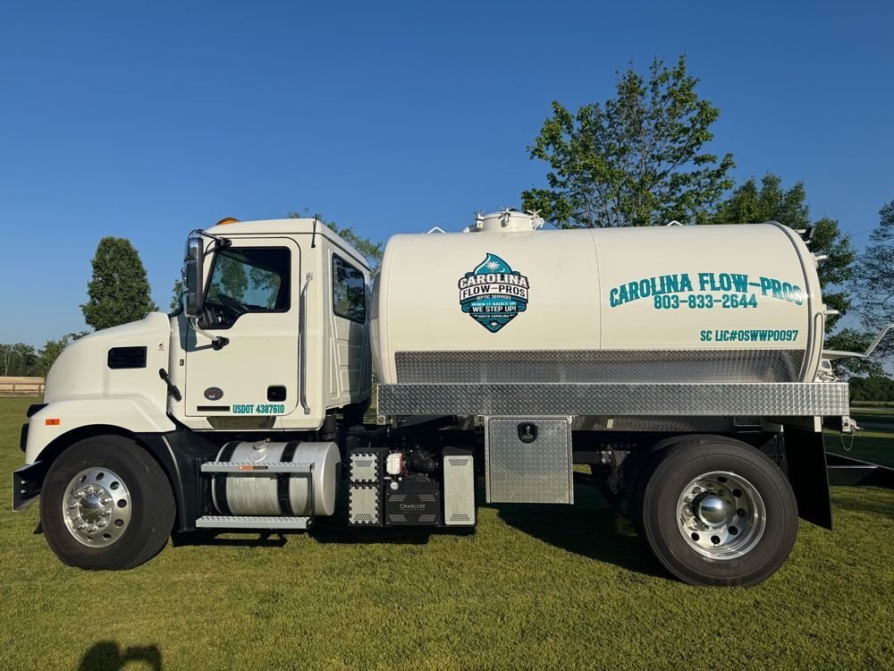 White septic tank truck with company logo, parked on grass. Blue sky.