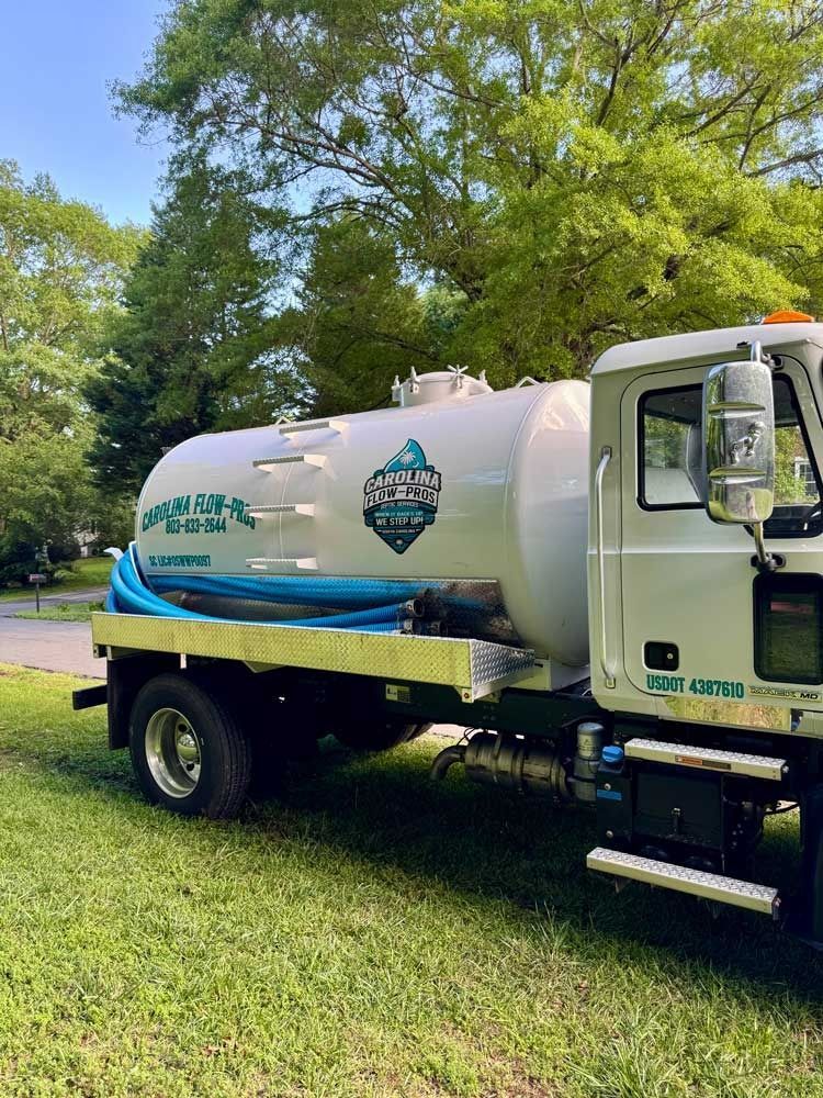 Septic tank truck with a large white tank, parked on grass.