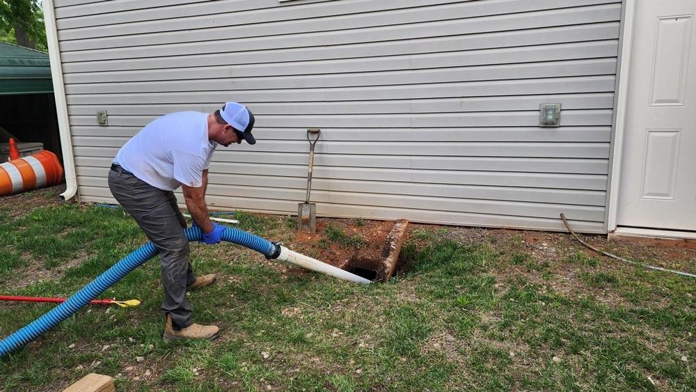 Man vacuums out a hole in the ground next to a building.