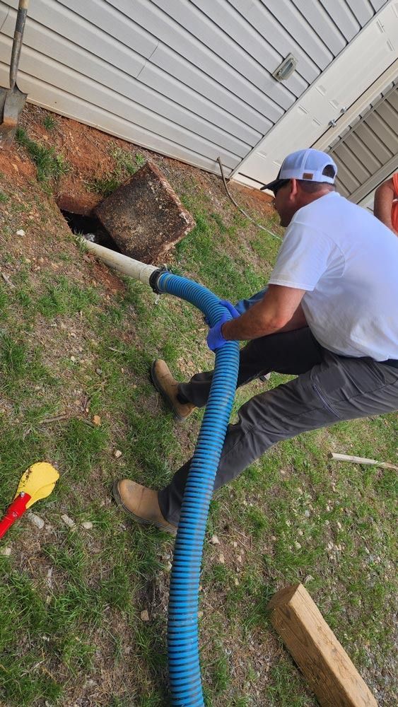 Man using a vacuum hose to clear a hole in the ground near a building.