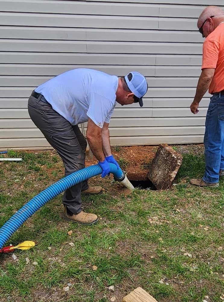 Man vacuuming a hole in the ground next to a building, another man watches.