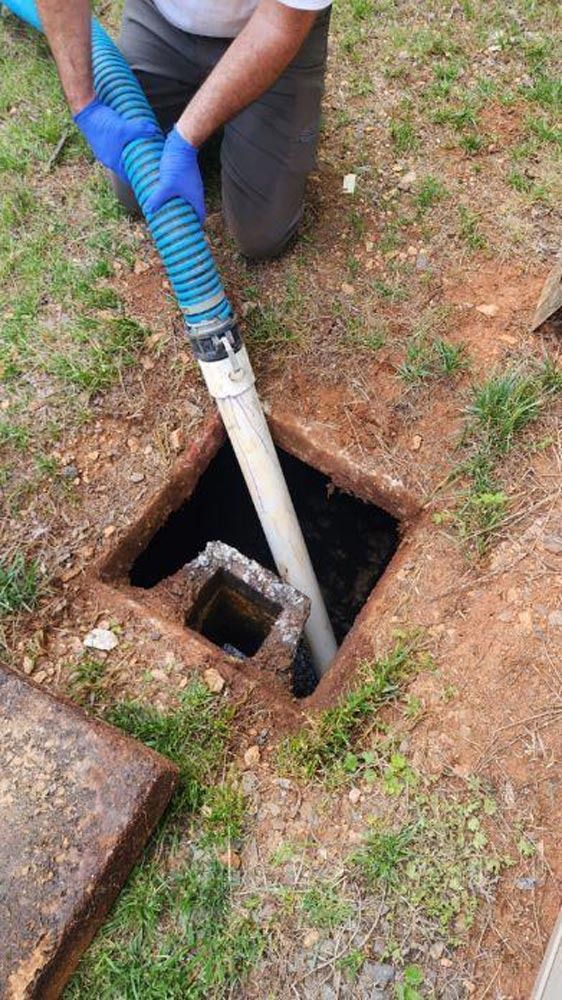 Person vacuuming a septic tank, using a hose to remove waste from an open ground access.