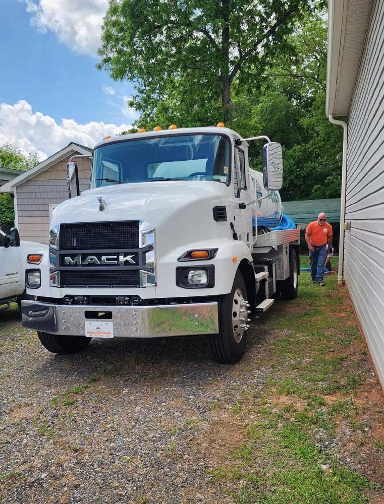 White Mack truck parked next to a building. A man walks near the truck on a sunny day.