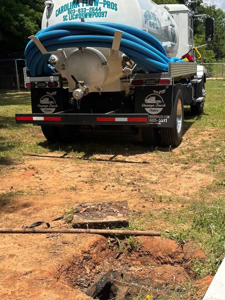A septic tank truck parked over a partially uncovered septic tank in a yard.
