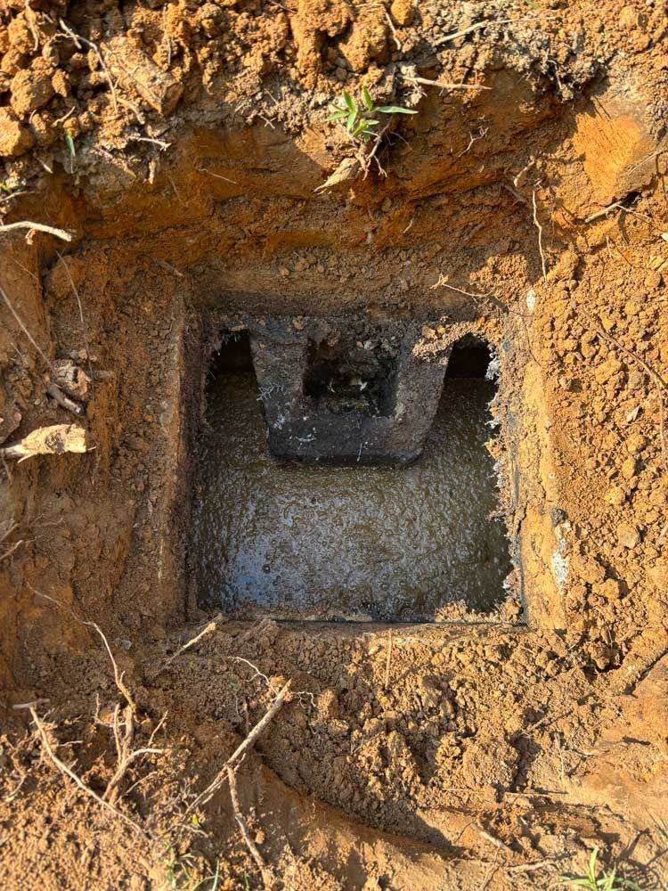 A square concrete box buried in dirt. The top is open, revealing the interior with dark shadows.