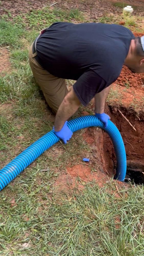 Man in blue gloves inserts blue hose into a dark hole in the ground.
