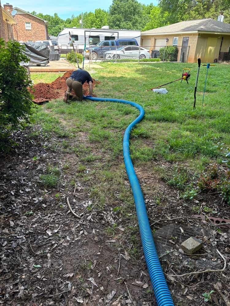 Man installing blue flexible pipe in backyard.