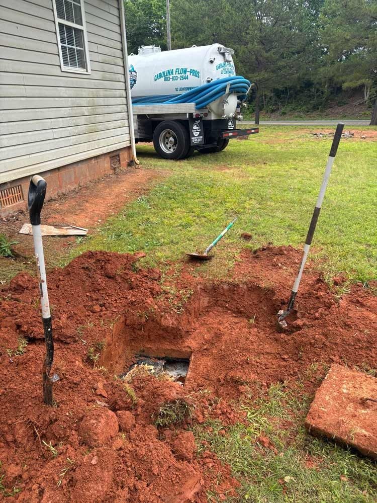 Septic tank being serviced; truck parked on grass, open hole, shovels, red soil.