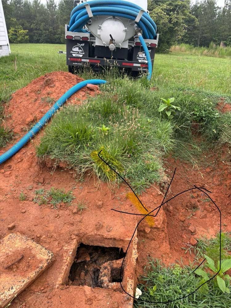 Septic tank being pumped; truck with hose, open access, red dirt, and green grass.