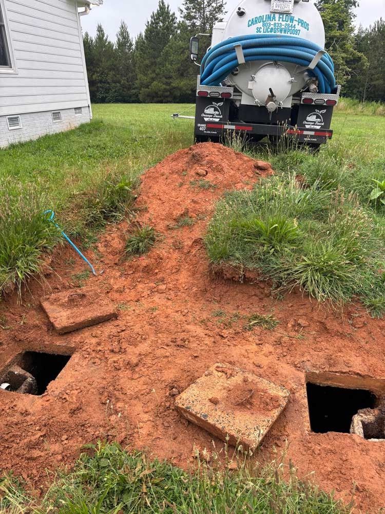 Septic tank service: truck parked, two open access points in dirt, grass, house in background.
