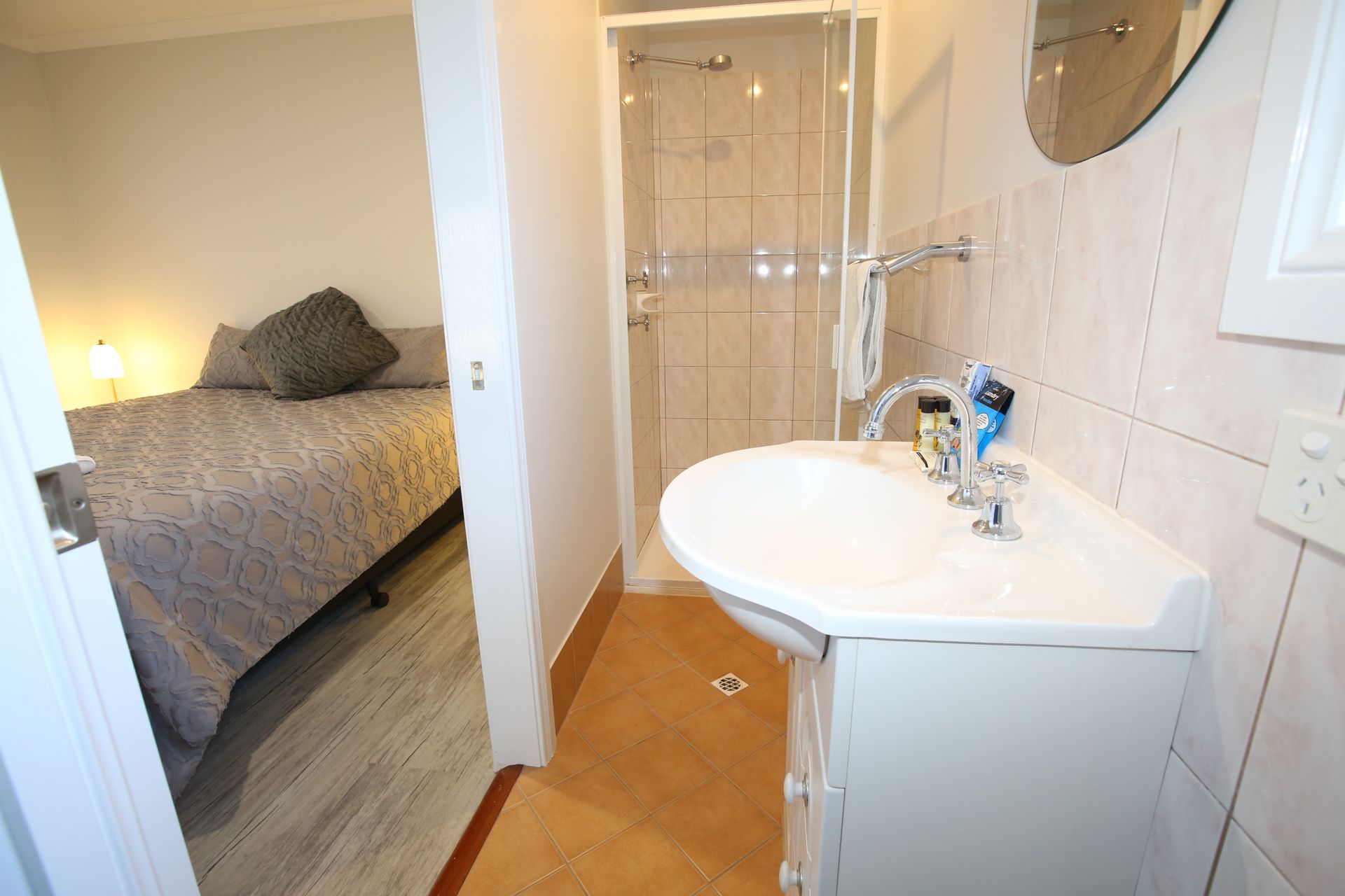 A bathroom with a sink and a shower next to a bedroom.
