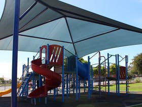 A playground with a red slide and a blue slide under an umbrella.
