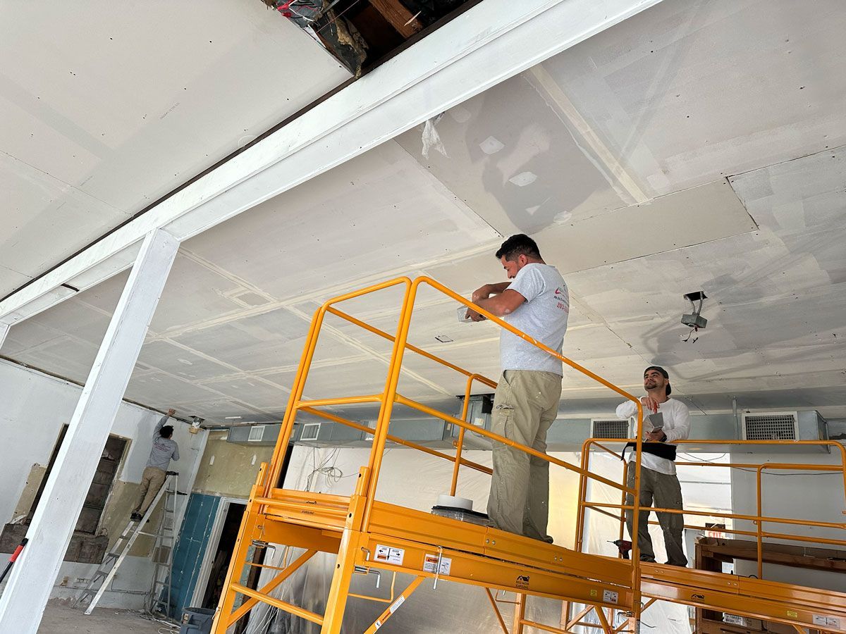 Two men are working on a ceiling on a scaffolding.