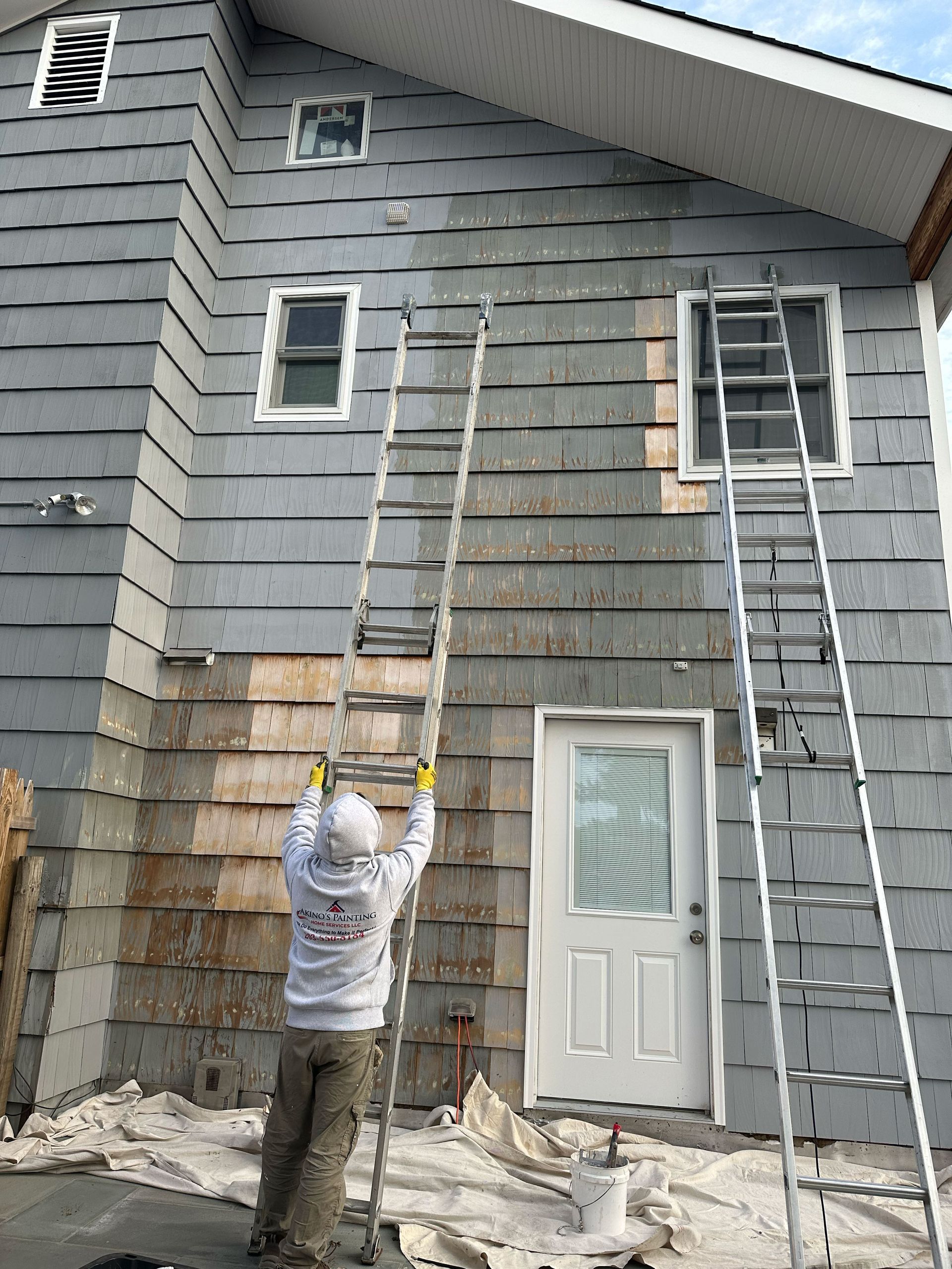 A man is standing on a ladder painting the side of a house.