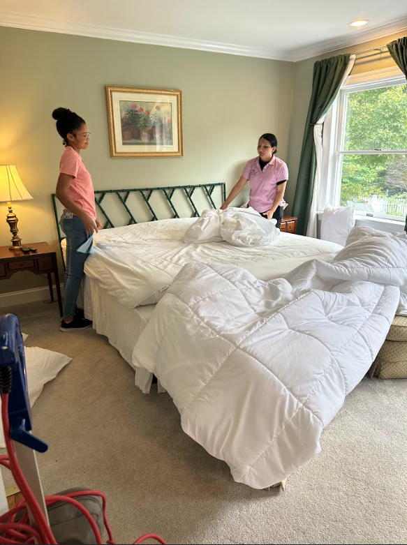 Two women are making a bed in a bedroom.