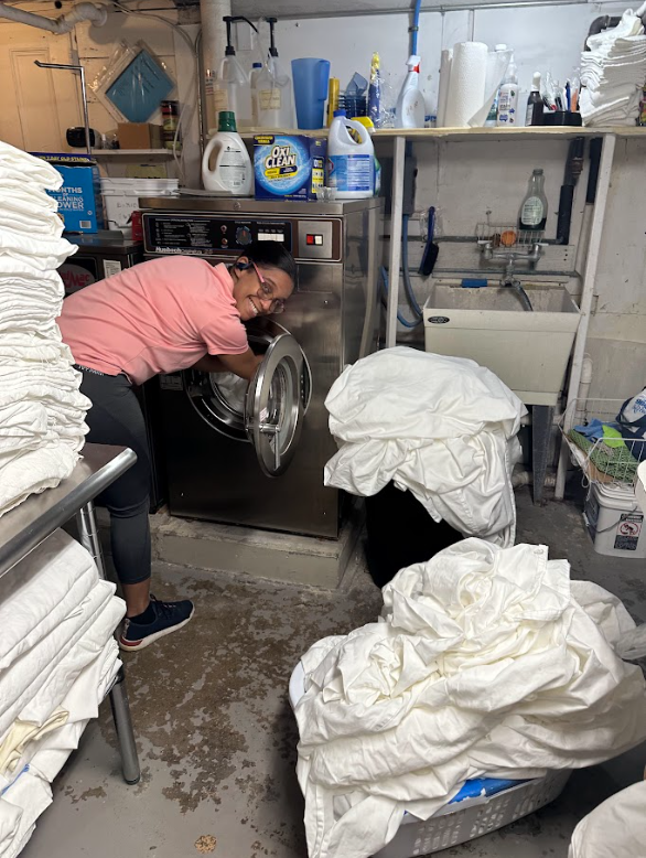 A woman is working on a washing machine in a laundromat.