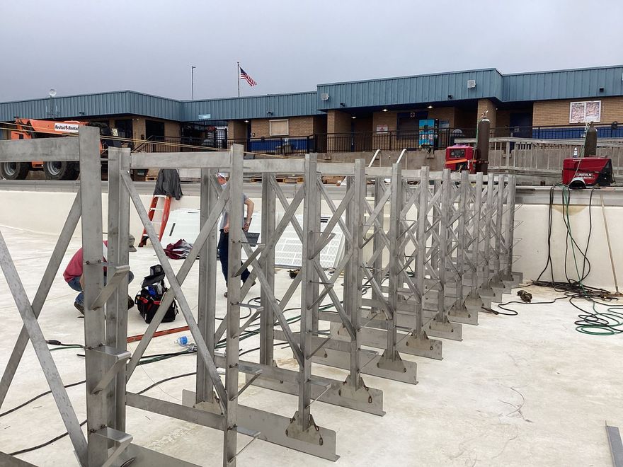Row of silver metal barriers in front of a building; construction workers in background.