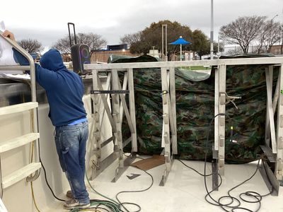 A person in blue hoodie working on a structure, potentially on a boat. Camo fabric is used.