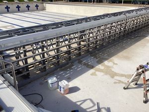 Construction of pool gutter system, gray metal frame, white concrete surround, blue lane markers visible.